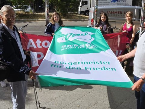 Clara Herrmann zeigt gemeinsam mit Aktivist*innen die Flagge der "Mayors for Peace" vor dem Rathaus in Friedrichshain