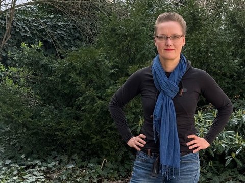 Romana Wittmer, Beauftragte für Gute Arbeit im Bezirksamt Friedrichshain-Kreuzberg, steht vor einer begrünten Fläche.