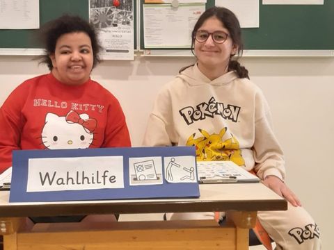 Yassmin und Sarah begrüßen alle Wähler*innen am Engang und erklären die Stimmzettel