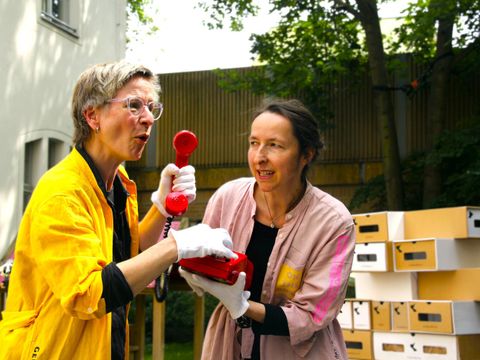 Die Spurensammlerinnen Rosa Kowalski und Coco Rosalski aus dem "MUSEUM der wandernden Erinnerungen" inspizieren ein rotes Telefon mit Drehscheibe