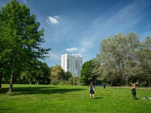 Menschen auf der Wiese im Fennpfuhl Park mit weißem Hochhaus im Hintergrund und Bäumen an den Seiten