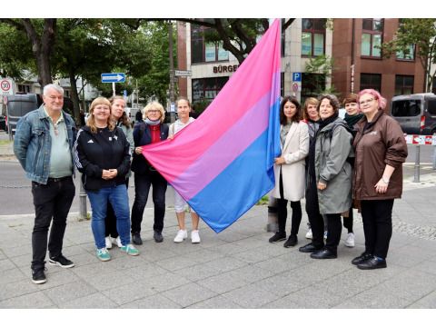 Mitglieder der AG Queer, die Diversity- und Queer-Beauftragte des Bezirksamtes, Sabine Pöhl, die stellvertretende Vorsitzende der BVV, Kerstin Zimmer, die Bezirksstadträtin Filiz Keküllüoğlu, Constanze Körner von LesLeFam e.V. und Dana Wetzel, BiBerlin e.V., bei der Flaggenhissung vor dem Rathaus. (Bild: Bezirksamt Lichtenberg)