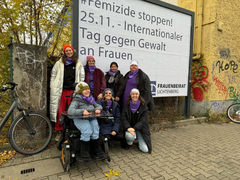 Mitglieder des Frauenbeirates Lichtenberg vor der Werbefläche mit dem Text: # Femizide stoppen! 25.11. Internationaler Tag gegen Gewalt an Frauen, in der Nähe einer Tankstelle in der Siegfriedstraße.