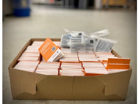 Karton mit Notfallkarten gegen Gewalt steht auf dem Boden. Im Karton liegen auch ein paar Karten mit Brailleschrift. (Bild: Bezirksamt Lichtenberg)