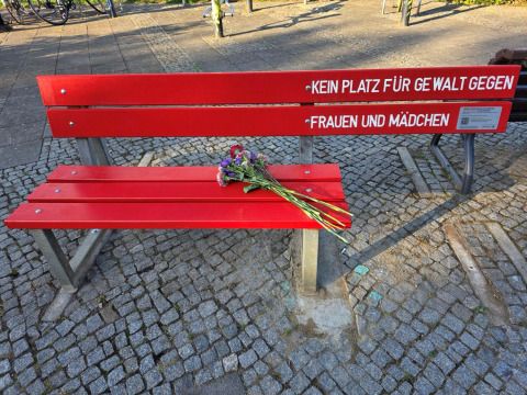 Einweihung der Roten Bank im Quartierspark Altenhofer Dreieck. Die Rote Bank hat auf der rechten Seite folgende Aufschrift: KEIN PLATZ FÜR GEWALT GEGEN FRAUEN UND MÄDCHEN. Neben der Schrift befindet sich ein Schild mit Hilfsnummern und einem QR-Code auf eine Seite mit Angeboten gegen Gewalt. (Bild: Frauenbeirat Lichtenberg)
