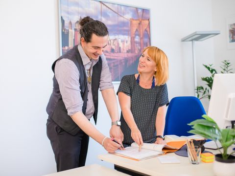 Ein Mann und eine Frau stehen an einem Schreibtisch und diskutieren freundlich über ein Schriftstück