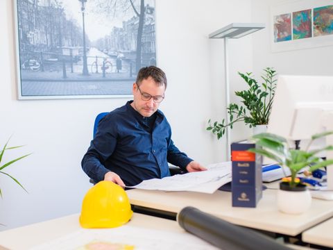Mitarbeiter sitzt vor einem Bauplan am Schreibtisch