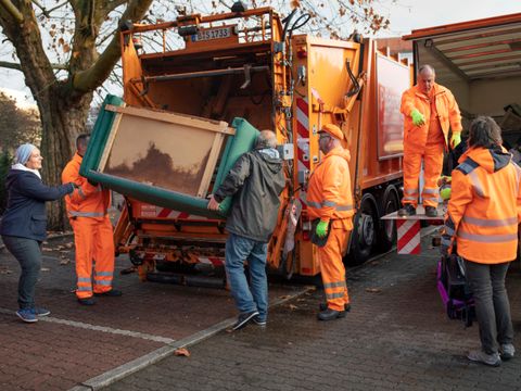 Gemeinsam entsorgen BSR und Anwohnende eine alte Couch direkt in ein Müllfahrzeug