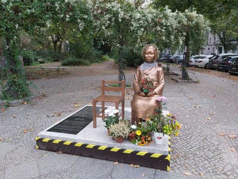 "Friedensstatue" zeigt eine sitzende FRau. Neben ihr steht ein weiterer Stuhl, der leer ist