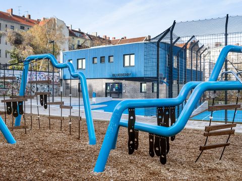 Spielplatz mit blauen Klettergeräten und grau-blauem Gebäude im Hintergrund