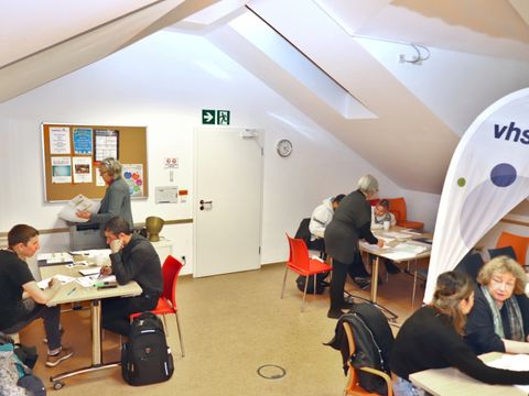 Mehrere Personen sitzen an Tischen in einem Raum und lernen