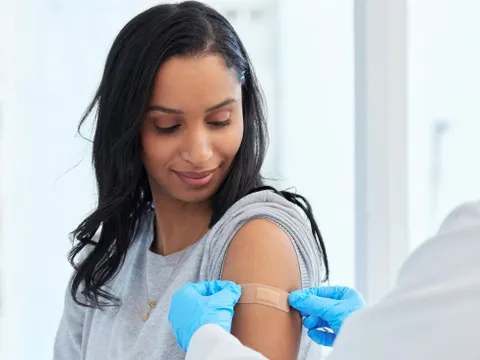 Healthcare, woman and doctor with plaster, vaccination and consultation in a hospital, cure and disease. Female patient, client and medical professional with care, vaccine and injection for safety