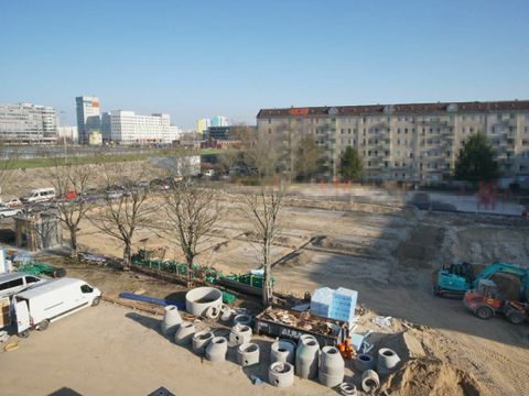 Leeres Baugrundstück vor Häuserblock mit Baggern und Baumaterialien am Rande