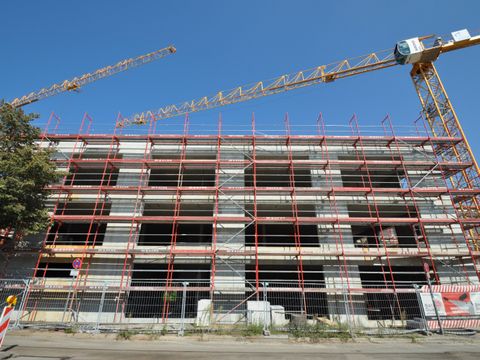 Schulneubau in Baugerüst mit gelbem Kran rechts daneben stehend