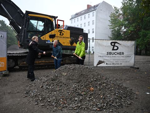 Drei Akteure machen ersten Spatenstich vor einem Bagger