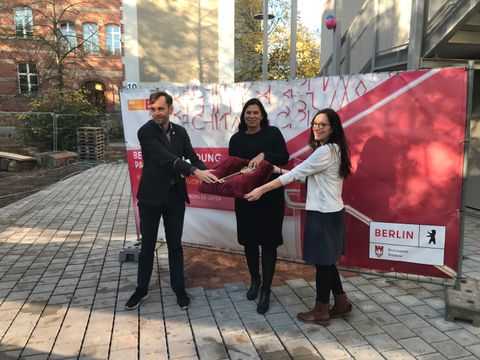 Symbolische Übergabe des Schlüssels für die Schule auf rotem Kissen von Schulbezirksstadtrat und Bildungssenatorin an die Schulleitung