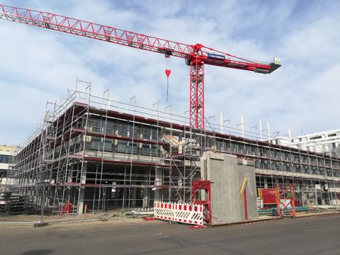 Schulrohbau in Baugerüst verkleidet vor rotem Kran