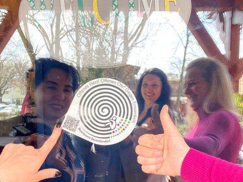 Einsamkeitsbeauftragte Katharina Schulz, Bürgermeisterin Demirbüken-Wegner und Geschäftsführerin vom Landhaus Schupke Melanie Niemann befestigen den Einsamkeitssticker an der Tür.