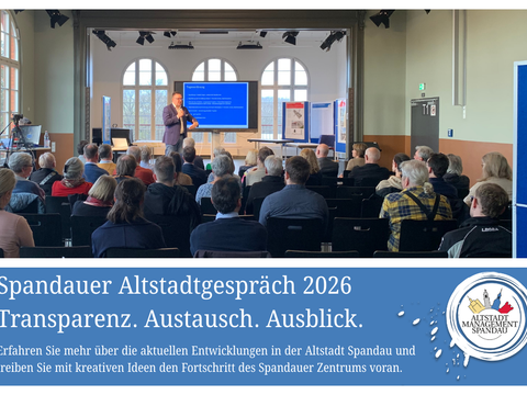 Vortragender steht vor Publikum in hellem Saal mit großen Fenstern und präsentiert vor blauem Bildschirm mit Text