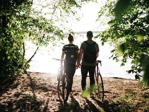 Pärchen mit Fahrrad am Uder mit Bäumen mit Blick auf den Wannsee