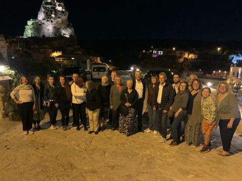 Eine Gruppe Menschen steht nachts auf einem Platz. Im Hintergrund ist eine beleuchtete Felsformation.
