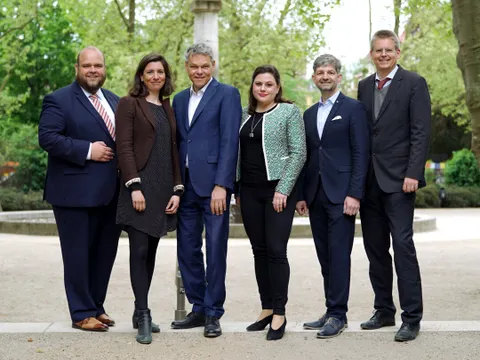 Sechs Personen stehen in einem Park vor einem Springbrunnen.