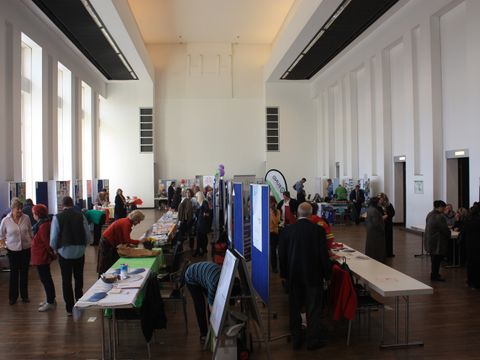 Großer Saal gefüllt mit Menschen und Ständen.