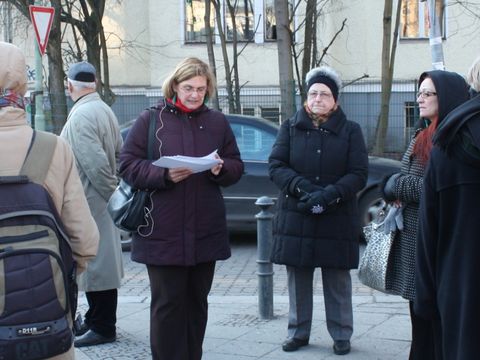 Eine Gruppe von Menschen, in der Mitte steht eine Frau und liest etwas vor.