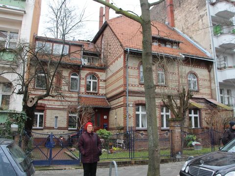 Eine Frau steht vor einer kleinen alten Villa mit einem kleinen Vorgarten.