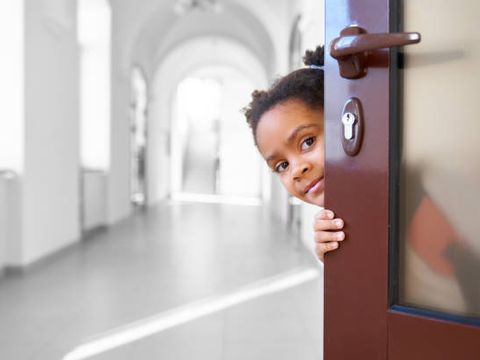 Pretty African girl hiding from opened door in school.