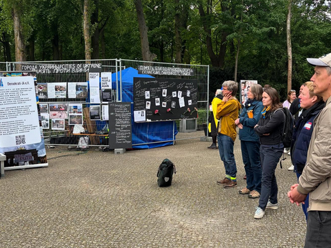 Bauzaun mit Mahnschriften und Gruppe von Menschen