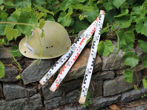 Bauhelm und Zollstock liegen auf einer Steinmauer