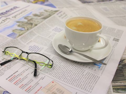 Abbildung einer Tasse, einer Brille und diverser Zeitungsblätter