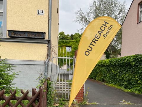 Eine Flagge vom Träger Outreach steht vor dem Eingangstor.