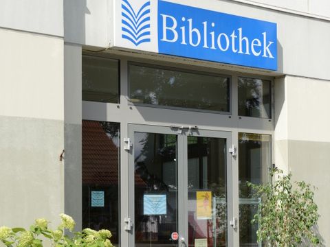 Der Eingang zur Bibliothek wird links und rechts von Pflanzen eingerahmt. Ein bequemer Stuhl und Tisch laden zum Verweilen ein.