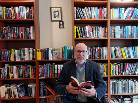 Das Foto zeigt Autor Frank Goyke sitzend vor einem gut gefüllten Bücherregal.
