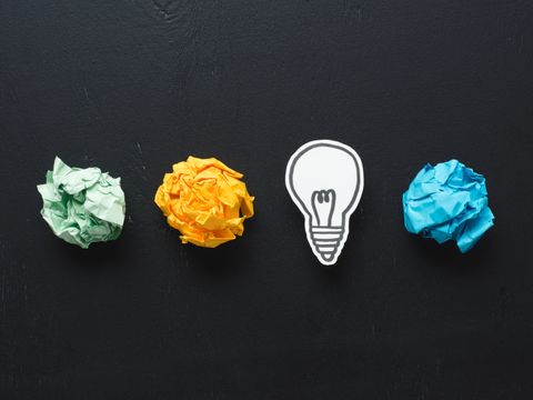 Top view of colorful crumpled paper balls and light bulb drawing on black background, ideas concept
