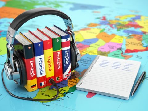 Bücher von Kopfhörer umschlossen auf einer Weltkarte, daneben Block und Stift