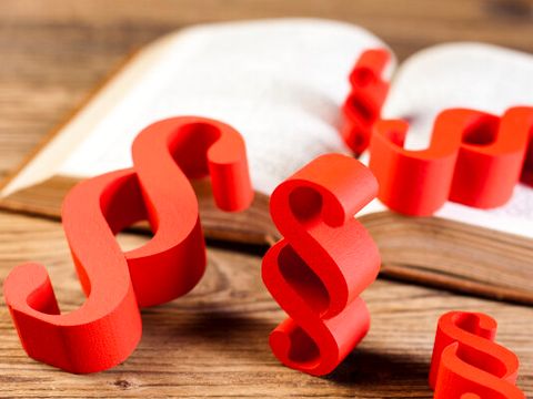 rote 3D-Paragraphenzeichen liegen auf einem/um ein Buch