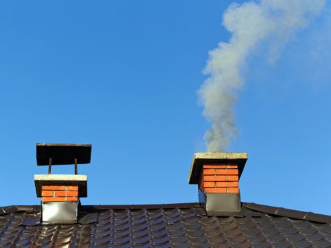 Rauch aus gemauertem Schornstein auf Dach gegen blauen Himmel