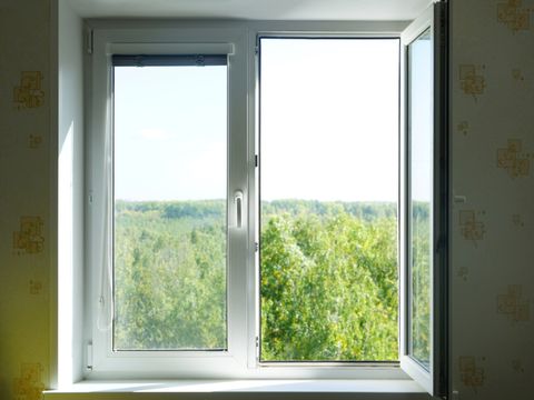 Offenes Kunststofffenster mit grünem Wald unter sonnigem Himmel auf einem Hintergrund