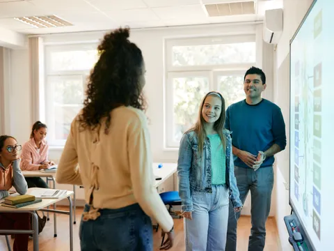 Schülerinnen und Lehrer stehen vor einem Smartboard