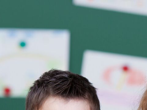 drei Kinder vor einer Tafel lehnen sich auf einen Stapel Bücher