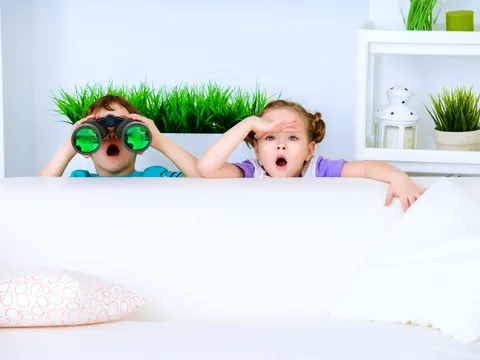 Zwei Kinder sitzen hinter einer Couch und entdecken etwas