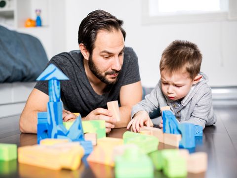 ein Mann und ein kleiner Junge liegen auf dem Boden und spielen mit Bauklötzern