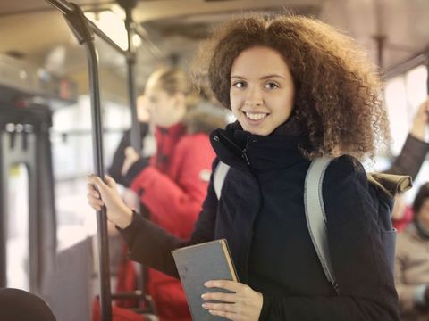 Lächelndes Mädchen mit einem Buch in der Hand und einem Rucksack auf ein autobus