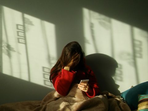 Frau schaut auf einem Bett auf ihr Handy