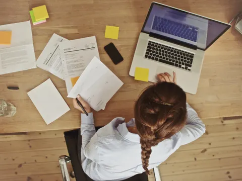 Frau arbeitend an ihrem Schreibtisch mit Dokumenten und Laptop