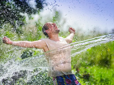 Mann im sommerlichen Garten wird mit Wasser bespritzt