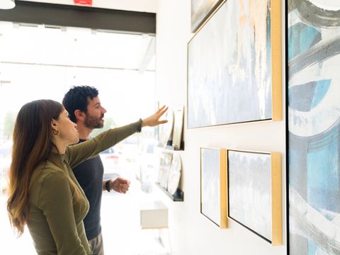 Gut aussehende junge Frau und erwachsener Mann entscheiden, welches Kunstbild sie für ihr Haus in der Ausstellung kaufen soll.